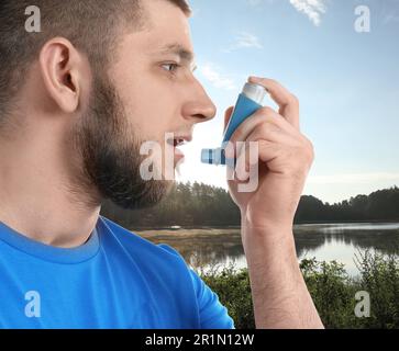 Man using asthma inhaler near lake. Emergency first aid during outdoor recreation Stock Photo