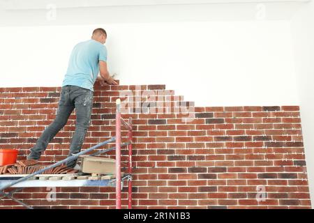 Professional builder gluing decorative bricks on wall indoors. Tiles installation process Stock Photo