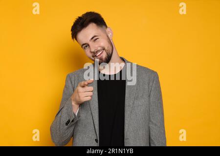 Handsome man in stylish grey jacket pointing at something on yellow background Stock Photo