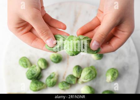 Woman separating leaves from fresh brussel sprouts at white table, closeup Stock Photo