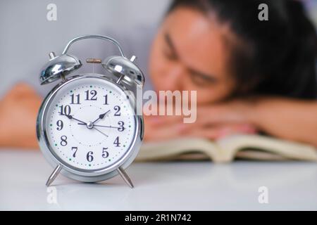 Tired Asian woman sitting at the desk reading a book in the living room. Stock Photo