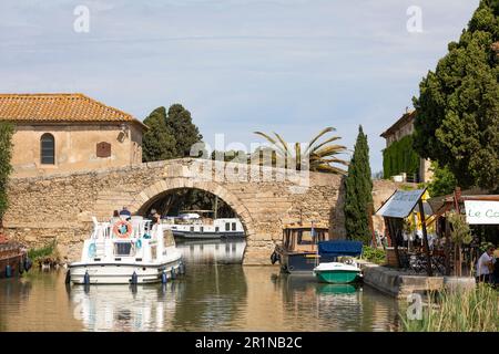 Family sailing a yacht, passing a bridge at the Canal du Midi in Homps, France Stock Photo