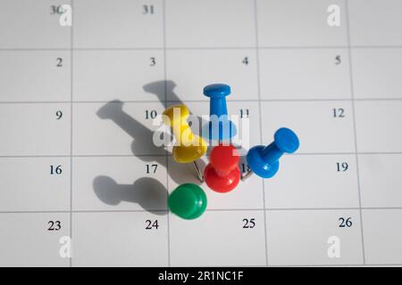 Multicolored pins on one date on a calendar. Busy and fully booked schedule concept. Stock Photo