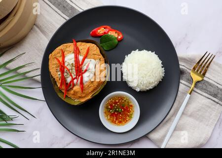 Steamed fish curry in banana leaf cups served with white rice - Famous Thai food called Hor Mok or fish Amok at top view on wooden background Stock Photo