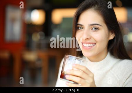 Happy woman holding soda glass in a bar looking at you Stock Photo