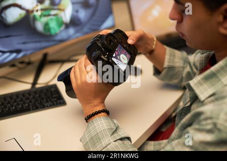 Young photographer examining photos on digital camera after shooting while sitting at his workplace in studio Stock Photo