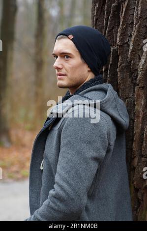 young man leaning against a tree in winter Stock Photo