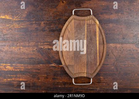 Wooden cutting board, oval, vintage, with iron handles on a wooden background. View from above Stock Photo
