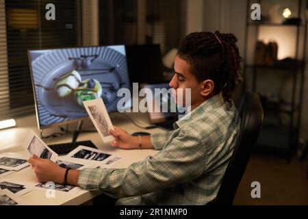 Young professional photographer examining old photos while sitting at his workplace with computer Stock Photo