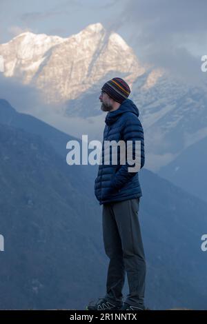 A bearded man overlooks the Himalayan peaks at dusk. Stock Photo