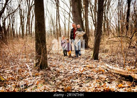 Father walks in woods with children holding baby and daughters hand Stock Photo