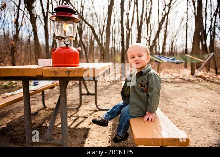 Smiling toddler boy sits on picnic table at campsite in fall Stock Photo