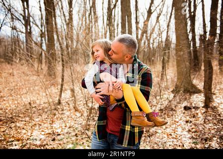 Loving father holds and kisses smiling daughter on cheek in Fall woods Stock Photo