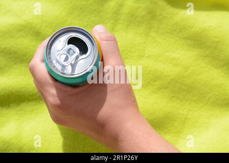 Woman holding aluminum can with beverage on yellow blanket, top view. Space for text Stock Photo