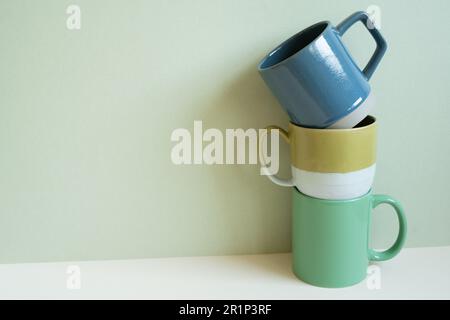 Stack of blue and green mug cups on white table. mint wall background. copy space Stock Photo