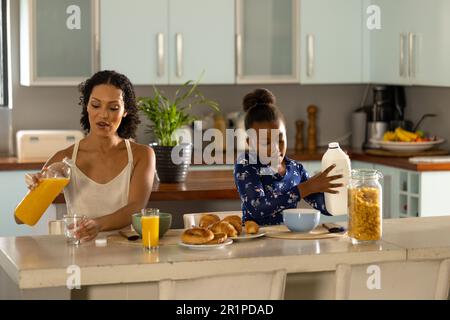 Happy african american mother and daughter sitting at kitchen island having breakfast together Stock Photo