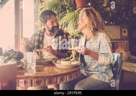 Adult happy couple eating brunch together sitting inside the cae bar restaurant. Casual people enjoynig food. Man and woman talking and smiling in indoor leisure activity. Job break Stock Photo