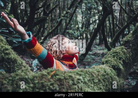 Woman celebrating nature lifestyle and outdoor leisure activity alone opening arms outstretching and looking the trees in forest green woods outdoor. Inner life balance mindful lifestyle female people Stock Photo