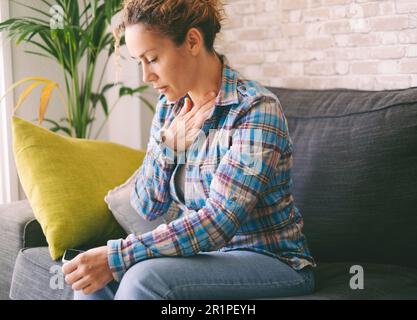 Pressure in the chest. Close-up photo of a stressed woman who is suffering from a chest pain and touching her heart area. People health bad condition and fear. One female touching chest worried Stock Photo