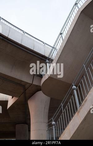 Low angle view of a staircase to a modern concrete bridge. Beautiful geometric background with a traffic overpass with grey railing and nobody on it Stock Photo
