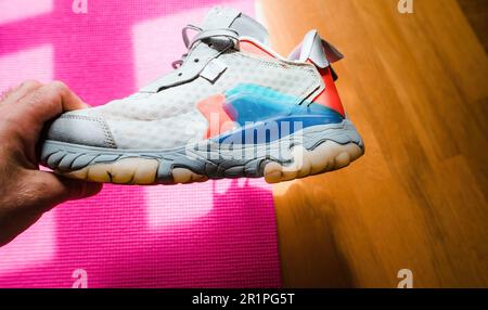 A man holds a damaged running shoe, inspecting the torn sole with his finger. He looks intently at it, as if assessing its need for repair. Stock Photo