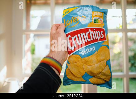 Paris, France - May 2, 2023: A mans hand holds a bag of Lorenz Salted Crunchips, ready to enjoy their salty snack goodness kitchen background Stock Photo