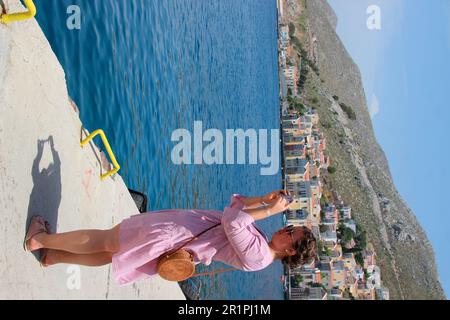 young woman taking cell phone photo on the harbor promenade of Simy, Greece, Stock Photo