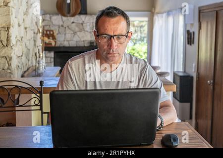 A man working at home, using a laptop computer, using internet, reading news, doing online shopping order for delivery, or studying with device online Stock Photo