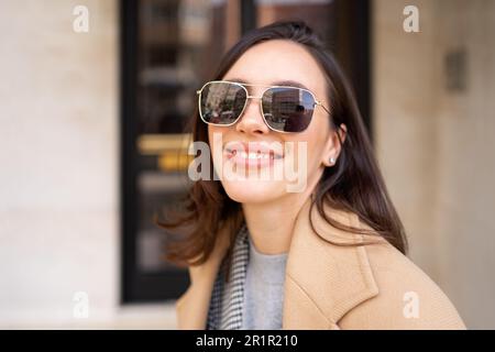 Streetstyle, street fashion concept: woman wearing trendy outfit walking in city. Cream trench coat, sunglasses Stock Photo