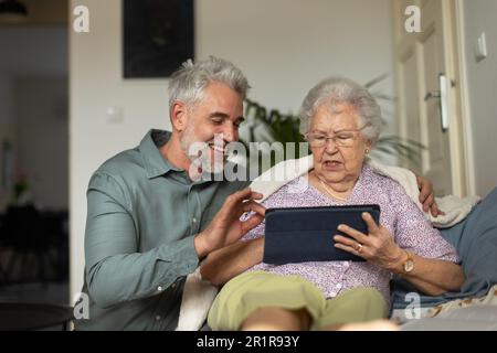 Mature man learning his senior mother working with digital tablet. Stock Photo
