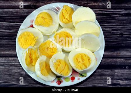 slices of hard boiled eggs previously made and cooked in hot boiling water, cut into pieces and served in a small plate isolated on a wooden backgroun Stock Photo