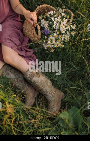 Woman sitting in a meadow in spring with a  basket filled with daisies, Belarus Stock Photo