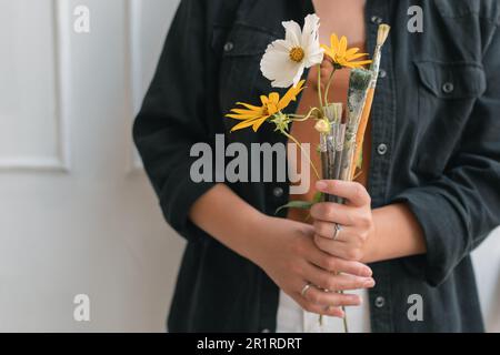 Close-up of young artist holding bouquet made of flowers and paint brushes in studio Stock Photo