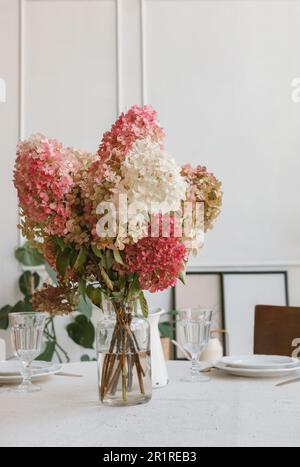 Vase of hydrangea flowers on a dining table set for dinner Stock Photo