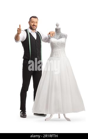 Tailor standing next to a bridal gown on a doll mannequin and gesturing thumbs up isolated on white background Stock Photo