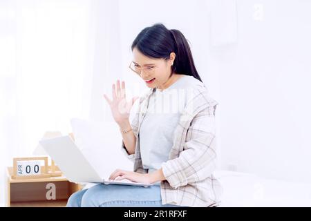 Smiling woman sitting on her bed making a video call on her laptop computer Stock Photo