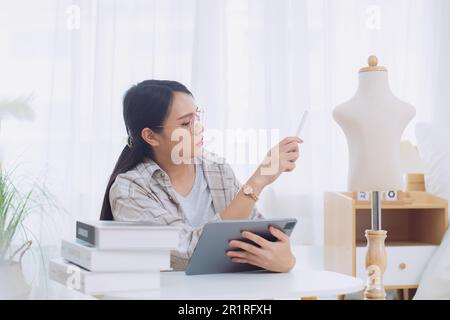 Smiling female fashion designer sitting at a table working on a digital tablet Stock Photo