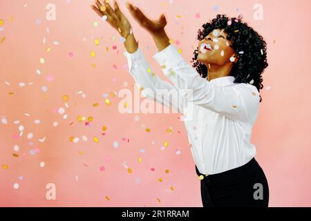 A special occasion - Portrait of a happy woman with arms out, smiling at confetti falling. Studio shot over pink background Stock Photo