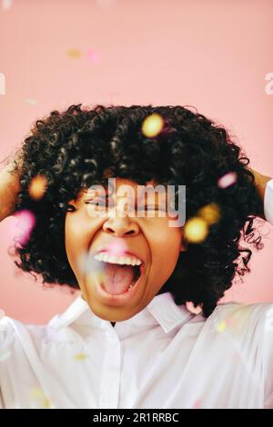 Happiness closeup portrait of cheerful beautiful black young adult woman wearing white shirt with open mouth and hands on hair under confetti rain cel Stock Photo
