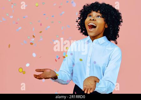 Portrait of a happy woman with open arms, smiling at confetti falling. Studio shot over pink background Stock Photo