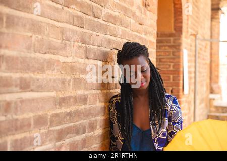 Portrait of an African woman with dreadlocks braid with umbrella parasol. Happy young woman feeling confident in her style. Fashionable woman standing Stock Photo