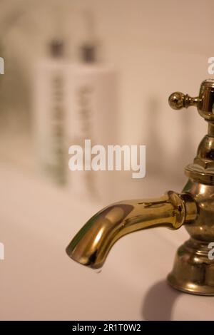 A set of brass traditional taps with some toiletries in the background Stock Photo