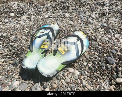 Beach scene with flip flop sandals lying on sea coquina shells and pebbles on the beach. Travel concept. Stock Photo
