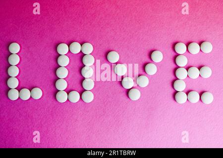 Beautiful inscription love made from white round smooth medical pills, vitamins, antibiotics and copy space on a bright purple pink background. Flat l Stock Photo