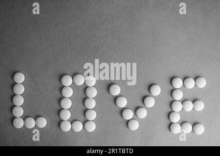 Beautiful inscription love made from white round smooth medical pills, vitamins, antibiotics and copy space on a black and white background. Flat lay. Stock Photo