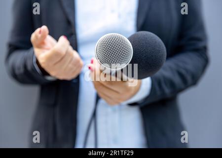 Female reporter holding microphone and gesturing during media interview. Freedom of the press concept. Stock Photo