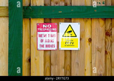 Close up of two warning signs attached to the fence of an isolated house, one general for CCTV, the other light-hearted and humorous. Stock Photo