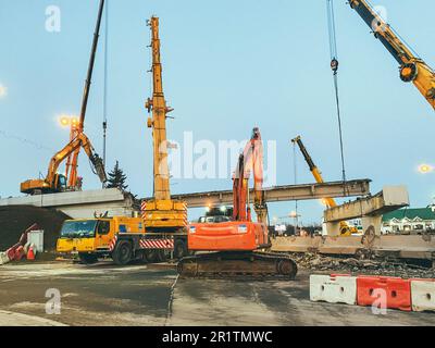 construction of a broken bridge on a busy road. the crane carries large concrete blocks. next to a plastic barrier of white and red color. Stock Photo