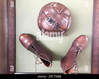 Old ancient antique retro hipster vintage brown leather stitched soccer ball and shoes, boots with laces for playing at the world championships on a g Stock Photo