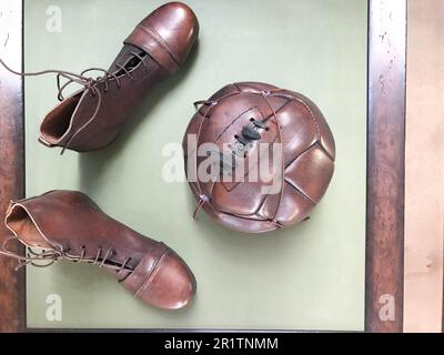 Old antique retro hipster vintage brown leather stitched soccer ball and shoes, boots with laces for playing on the grass. Stock Photo